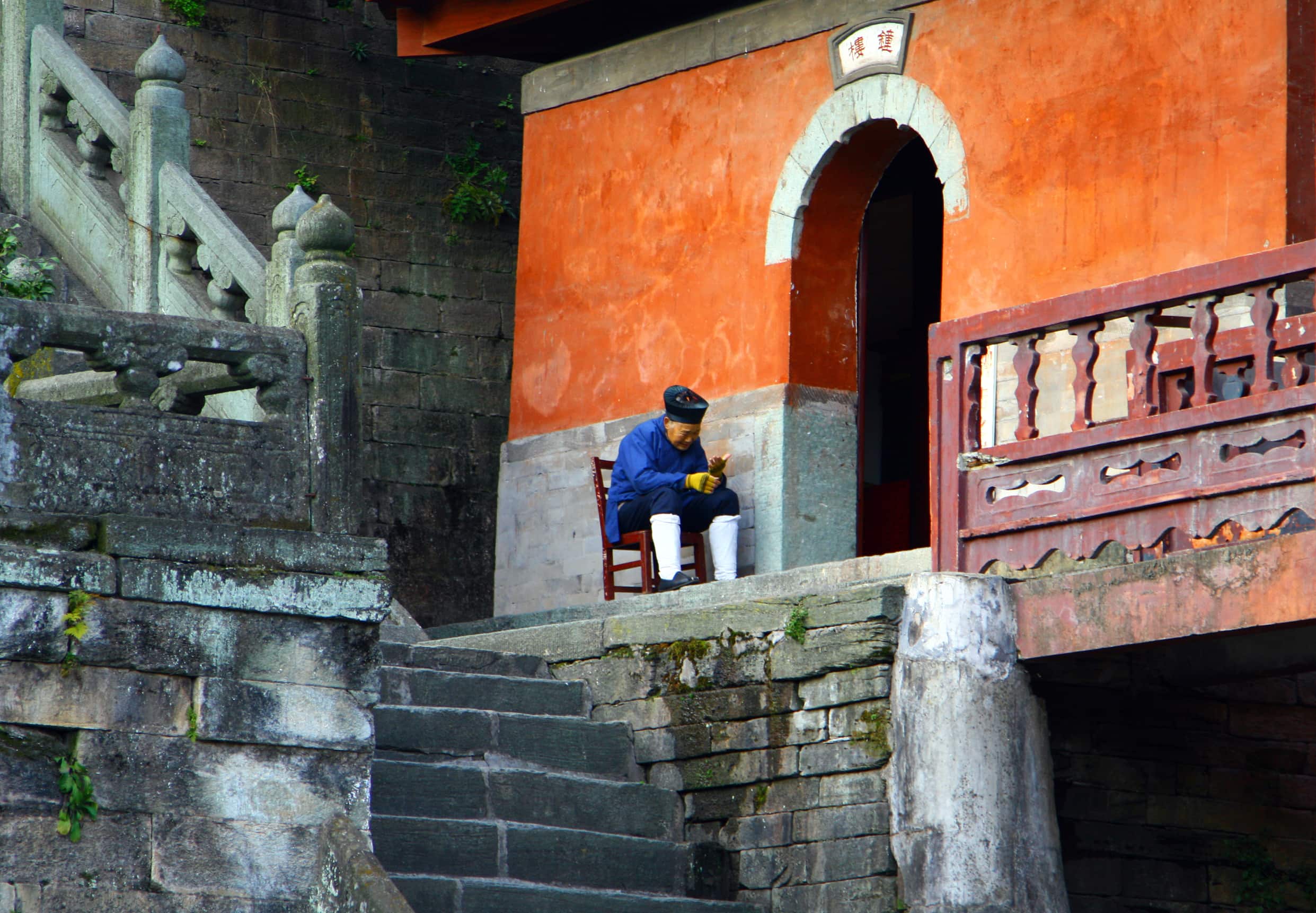 Elderly taoist monk sitting at the entrance to Purple Cloud Temple in Wudang Mountains, Hubei province Elderly taoist monk Purple Cloud Temple | Fighting Arts Health Lab